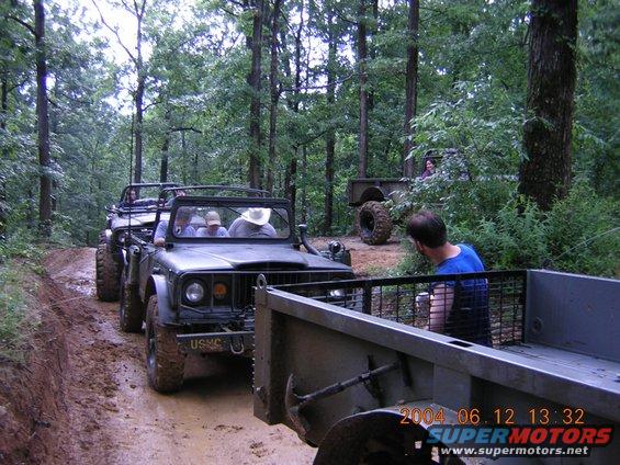 Military-style off-road vehicles on a muddy forest trail, front vehicle has USMC marking
