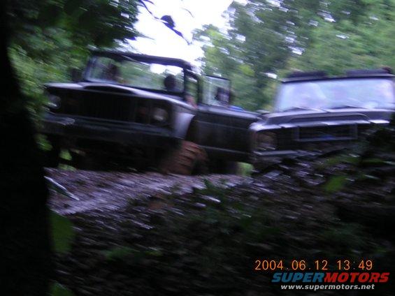 Two dark-colored off-road vehicles navigate a muddy trail in a forest