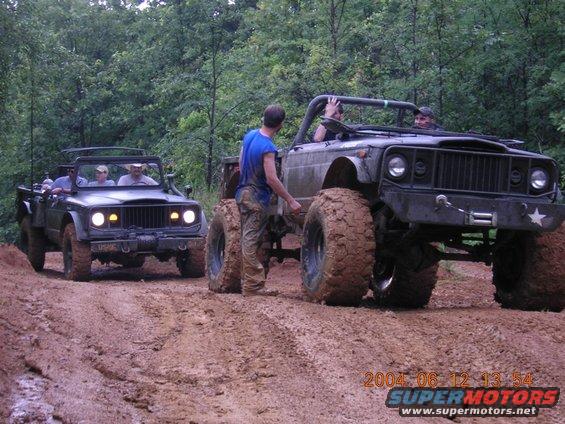 Two lifted Jeeps covered in mud on a trail, one in front of the other