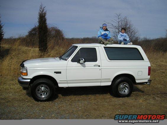 White 1996 Ford Bronco SUV, side view, with two children sitting on the roof