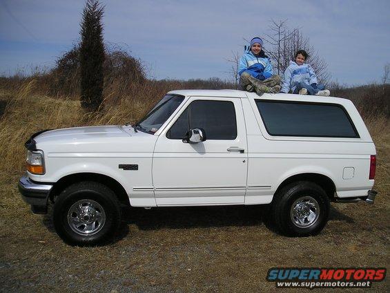 White 1996 Ford Bronco side view with two children on the roof