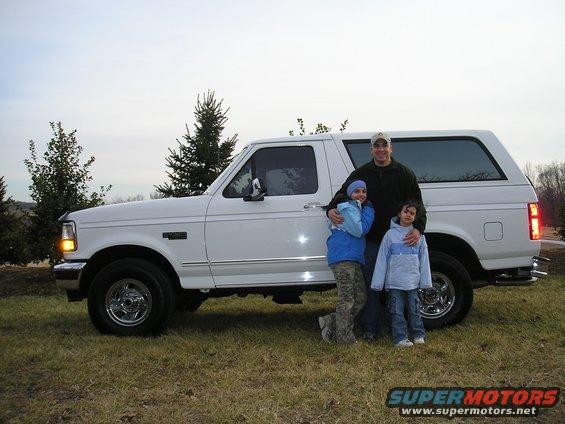 1996 Ford Bronco parked on grass with a man and two children standing next to it