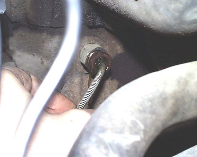 Close-up of a hand holding a metal cable connected to an engine component, with hoses visible
