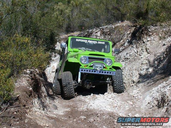 Green off-road vehicle with a winch and custom bumper navigating a rocky trail