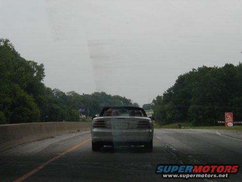 Rear view of a silver convertible driving on a highway, possibly a Ford Mustang