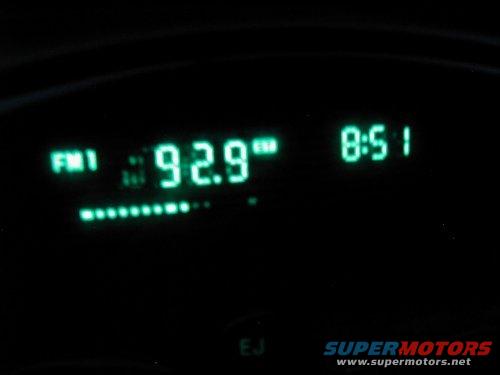 Car dashboard display showing FM1 92.9 and 8:51, with SUPERMOTORS.NET text at the bottom