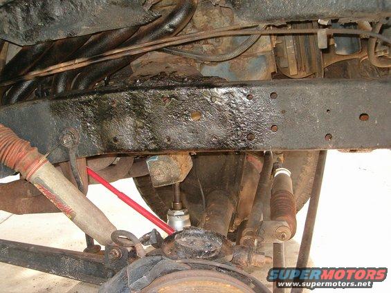 Undercarriage view of vehicle suspension and frame with visible rust and oil