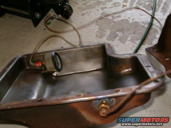 Oil pan with a small gauge attached, wires running to it. Some green fluid is visible