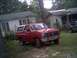 1985 Ford Bronco - A red Ford Bronco with a white top and bull bar sits in a grassy yard next to two houses.