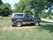 1986 Ford Bronco - This Ford Bronco is parked on a grassy area with trees and a road visible in the background.