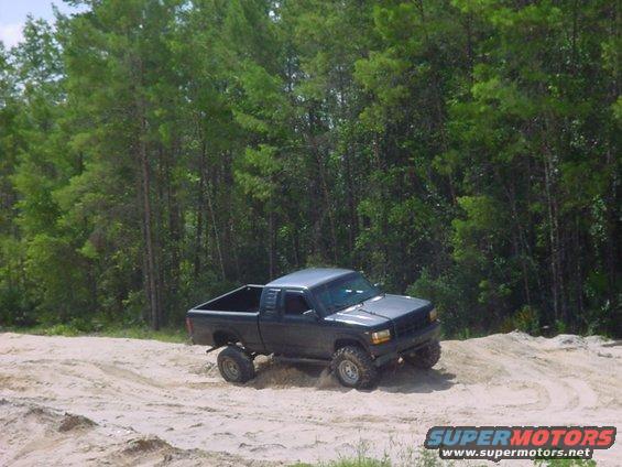 Dark gray pickup truck with off-road tires driving on a sandy track