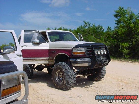 Lifted 1992 Ford Bronco with maroon stripe and bull bar, parked next to another truck