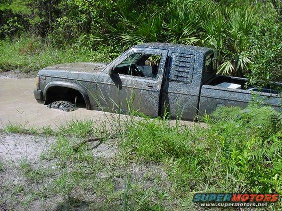Mud-covered pickup truck stuck in water with front wheel submerged