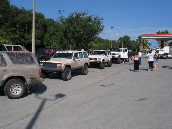Several lifted SUVs, including a white Jeep Cherokee XJ with a sticker on the windshield, lined up at a gas station
