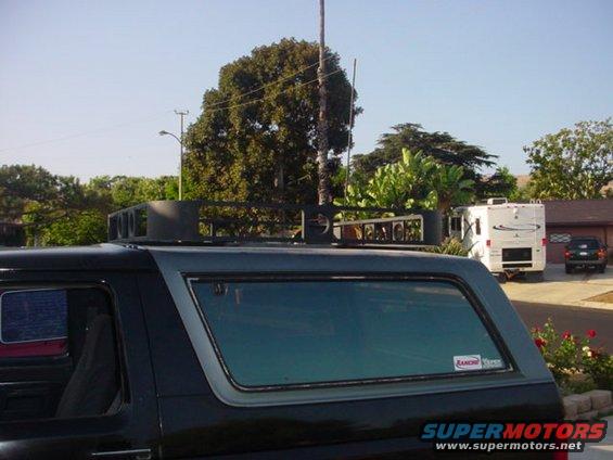 Black Ford Bronco side view with a custom roof rack. A white RV and a dark SUV are parked in the background