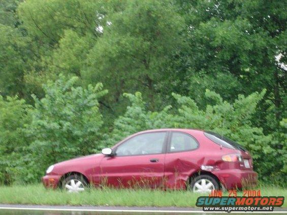 Red sedan parked on grassy shoulder with significant damage to the rear passenger side quarter panel
