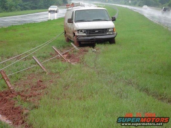 White cargo van off-road, front bumper damaged, pulled by wires attached to fence posts