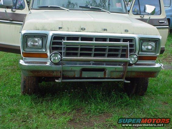 Front of a beige Ford truck with its grille and headlights visible. Another vehicle is partially seen to the right