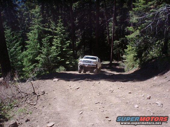 White 1992 Ford Bronco driving on a dirt road in a forest
