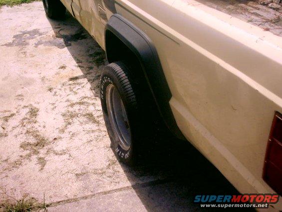 Side view of a beige Jeep Comanche pickup truck, showing the rear wheel well and part of the bed