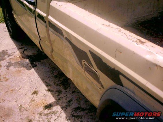 Side view of beige pickup truck bed with dark stripe graphic and visible rust