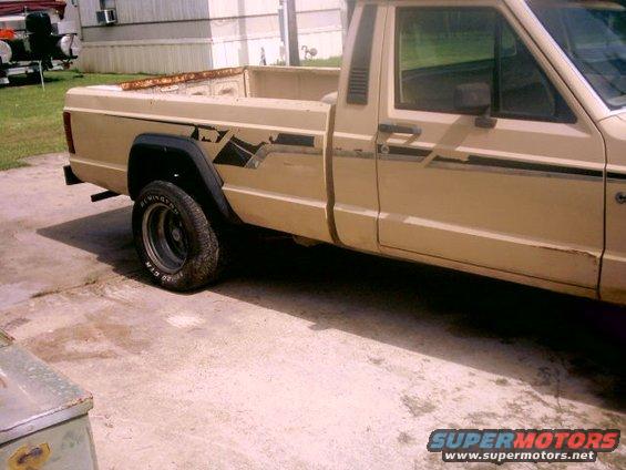 Tan pickup truck with black fender flares and side graphics, viewed from the side
