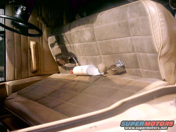 Interior shot of a vehicle's front bench seat, showing worn upholstery and a seatbelt. A white can is on the seat