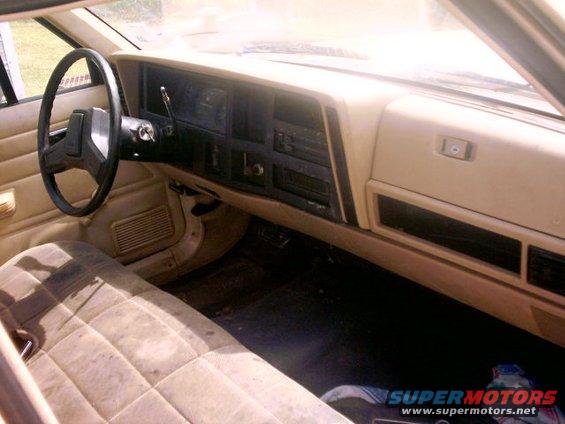 Tan interior of a car with a quilted seat, dashboard, and steering wheel. The "SUPERMOTORS" logo is visible