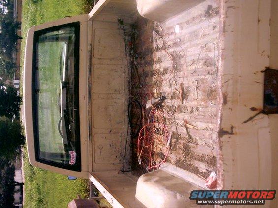 Interior of a pickup truck bed showing exposed wiring and a dirty floor. The cab window is visible
