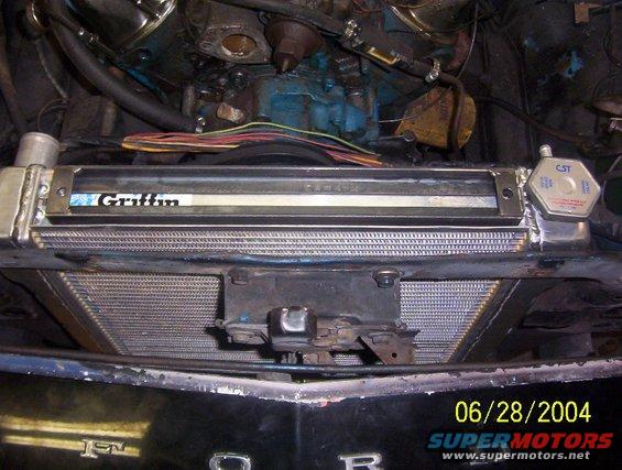 Close-up of a car's radiator with a Griffin logo and CST cap, showing engine components and wiring