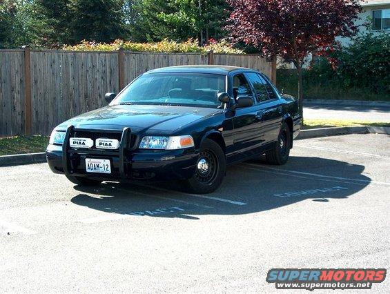 Black 2001 Ford Crown Victoria police car with a push bar and PIAA lights parked in a lot