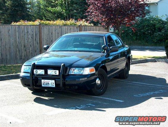 Dark blue 2001 Ford Crown Victoria police car with a push bumper and light bar, parked in a lot