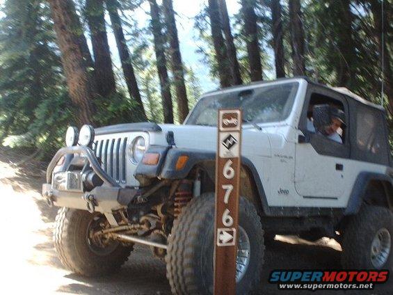 White Jeep Wrangler with off-road tires and bumper parked on a dirt trail