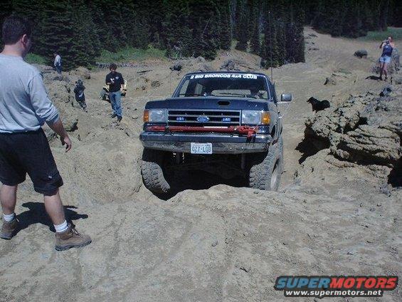 Ford Bronco navigating rocky terrain, with people watching