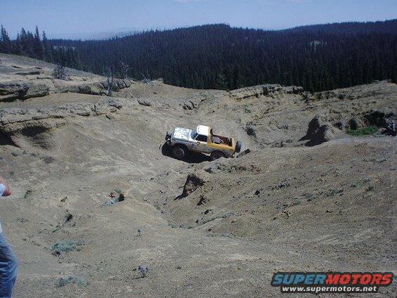 1978 Ford Bronco driving off-road on a dirt hill, white and yellow exterior, spare tire on rear