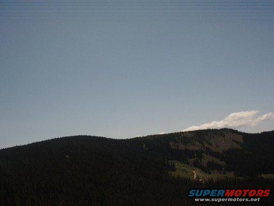 Mountain landscape with a dirt road winding through trees under a clear blue sky