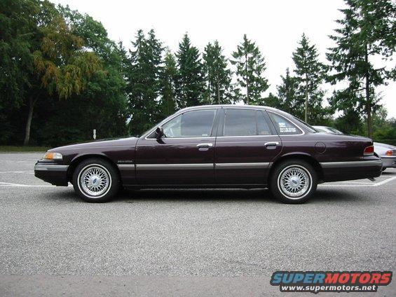 Dark purple Ford Crown Victoria parked outside with trees in the background