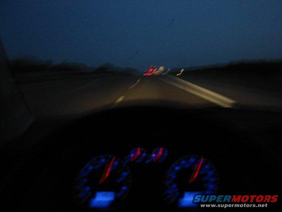 Dashboard gauges at night with road visible through windshield