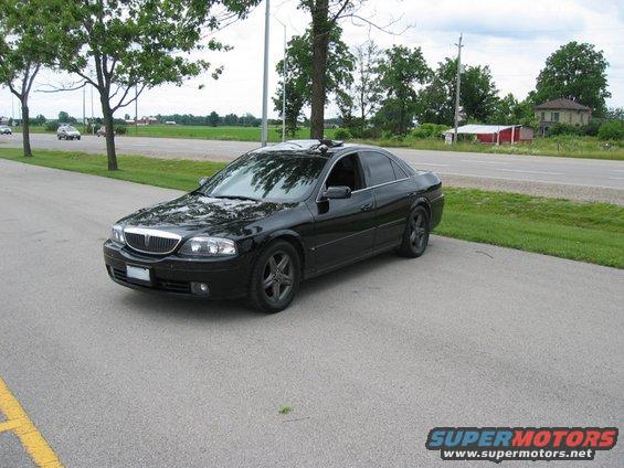 Black sedan parked on asphalt, front 3/4 view. Grille and headlights visible