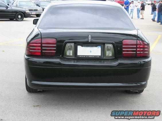 Rear view of a black Lincoln Town Car with a "LINCOLN LS OWNERS CLUB" license plate frame. Other cars are visible in the background