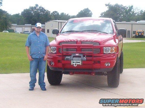 Man standing next to a red Dodge Ram pickup truck with a brush guard and winch