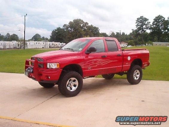 Red pickup truck with aftermarket bull bar and large tires, parked on concrete