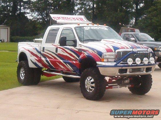 Lifted pickup truck with red, white, and blue graphics and 'SkyJacker' sign on top