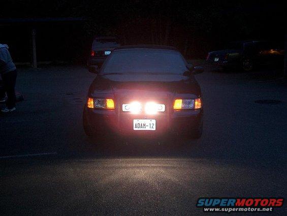 2001 Ford Crown Victoria front view, auxiliary lights on, license plate ADAN-12. Another vehicle visible in background
