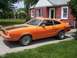 1978 Ford Mustang II - This orange coupe with racing stripes is parked in front of a brick house.