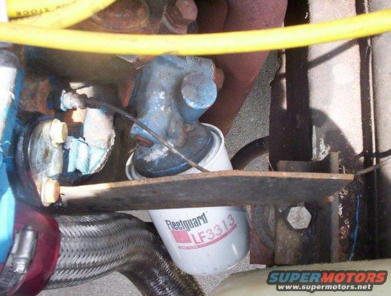 Fleetguard LF3313 oil filter attached to engine block with yellow hose and exhaust pipe visible