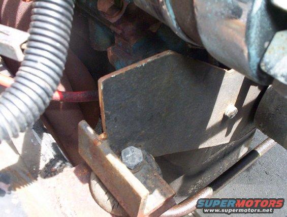 Close-up of a metal bracket bolted to an engine block, with a ribbed hose nearby
