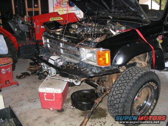 Toyota Land Cruiser with hood open, engine exposed, in a garage. Red Branson tractor in background