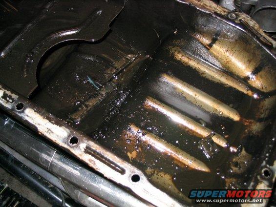 Dirty oil pan with sludge and debris, showing internal ribs and bolt holes