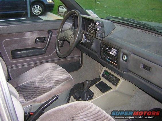 Interior view of a car showing dashboard, steering wheel, seats, and center console. A 'SUPERMOTORS' watermark is visible